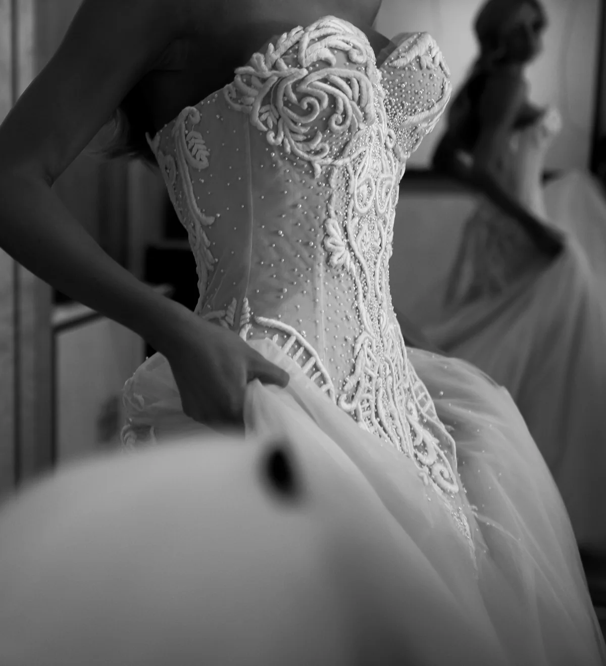 Bride being fastened into a beaded corset gown, her reflection in the mirror behind